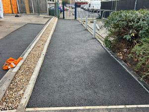 New asphalt pathway with gravel drainage channel, bollards, and perimeter fencing at Stratford car park