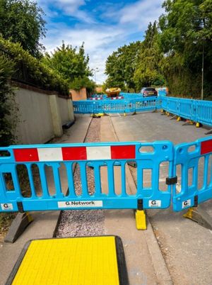Anstey Lane section cordoned off with blue safety barriers and a yellow trench cover plate during the active utility trenching programme in Alton