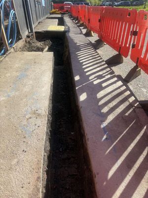 Freshly excavated LV cable trench alongside a building frontage on Aycliffe Road, Borehamwood, protected by orange portable safety barriers