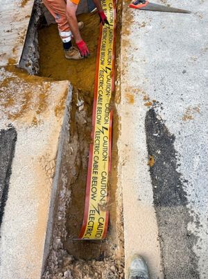 Construction operative placing yellow Caution Electric Cable Below warning tape inside a freshly dug trench on Anstey Lane, Alton, during electrical trenching