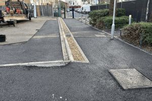 Aerial view of new asphalt car park surfacing with drainage channel, street lighting, and perimeter fencing at UEL Stratford