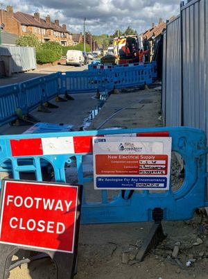 Blue safety barriers, Footway Closed signage, and an electrical supply works notice on Aycliffe Road, Borehamwood, during LV network installation