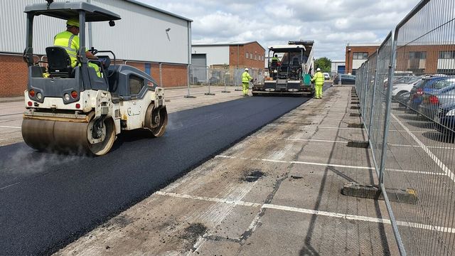 Asphalt resurfacing on a commercial estate car park with a paver and tandem roller inside a segregated work zone