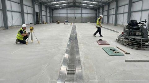 Food-grade concrete floor laid to falls with a stainless steel channel drain and a worker checking levels with a laser