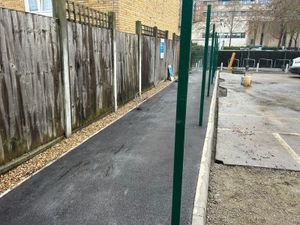Newly surfaced footpath alongside green fence posts and wooden perimeter fencing during car park construction