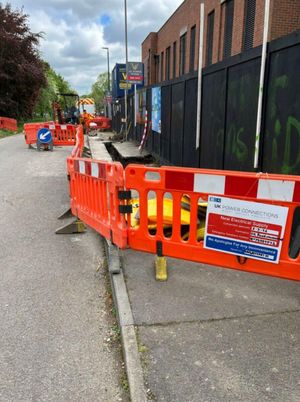 Open LV cable trench protected by orange portable safety barriers on Aycliffe Road, Borehamwood, with electrical supply works signage in the background