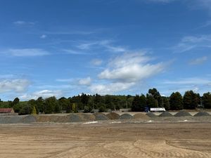 Wide view of Copart Dunfermline construction site with excavator performing earthworks on gravel surface under overcast skies