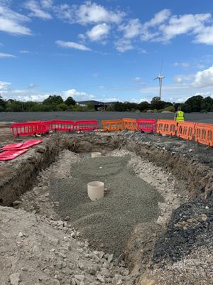 SPEL tanks being installed underground in a gravel-filled trench with safety barriers and a wind turbine visible at Copart Dunfermline