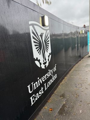 University of East London branded construction hoarding with illuminated signage at the Stratford project site
