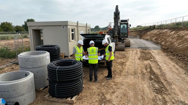 Civil engineering workers reviewing an infrastructure works package beside materials and plant on a UK construction site
